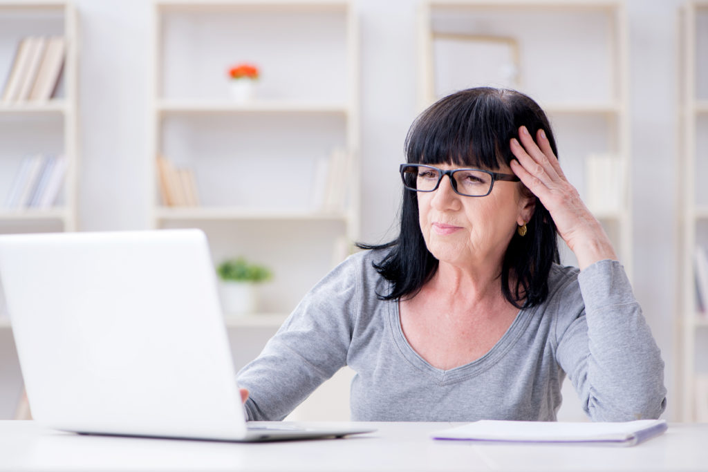 An older woman concentrates on her laptop before her on the desk.